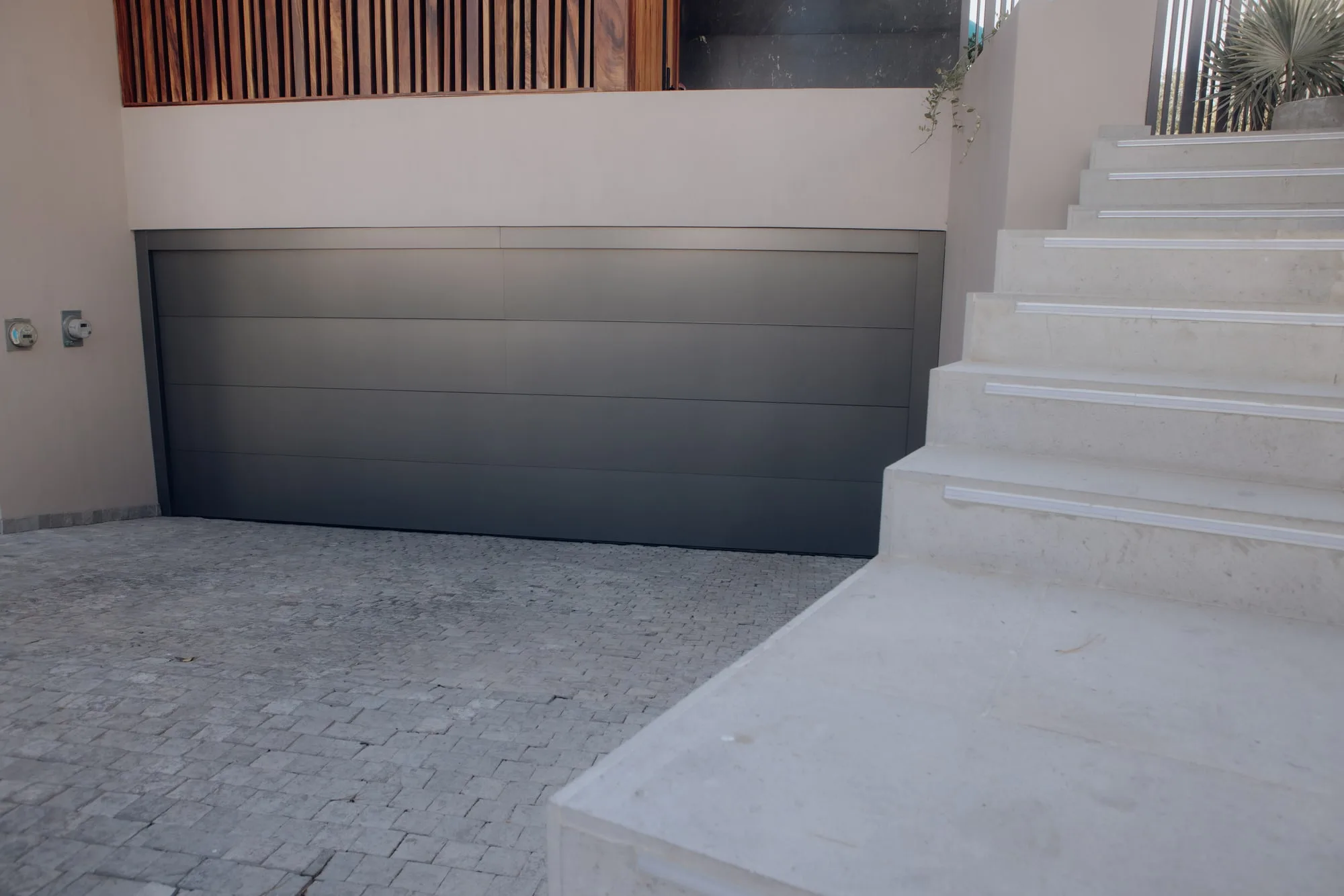 Portón ascendente de aluminio gris oscuro con paneles horizontales, junto a una escalinata de piedra clara