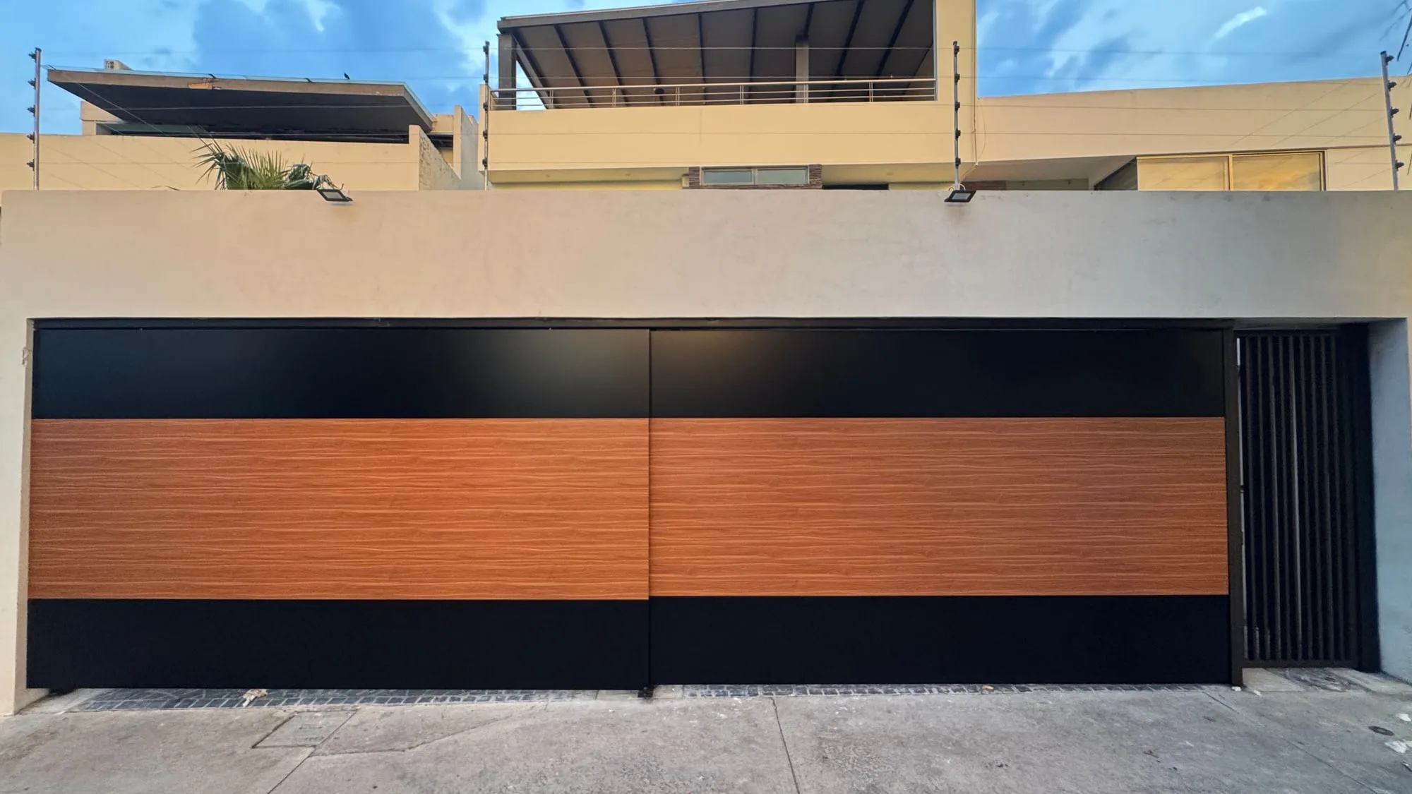 Portón corredizo negro con franja horizontal de madera, cerrando el acceso de una casa contemporánea