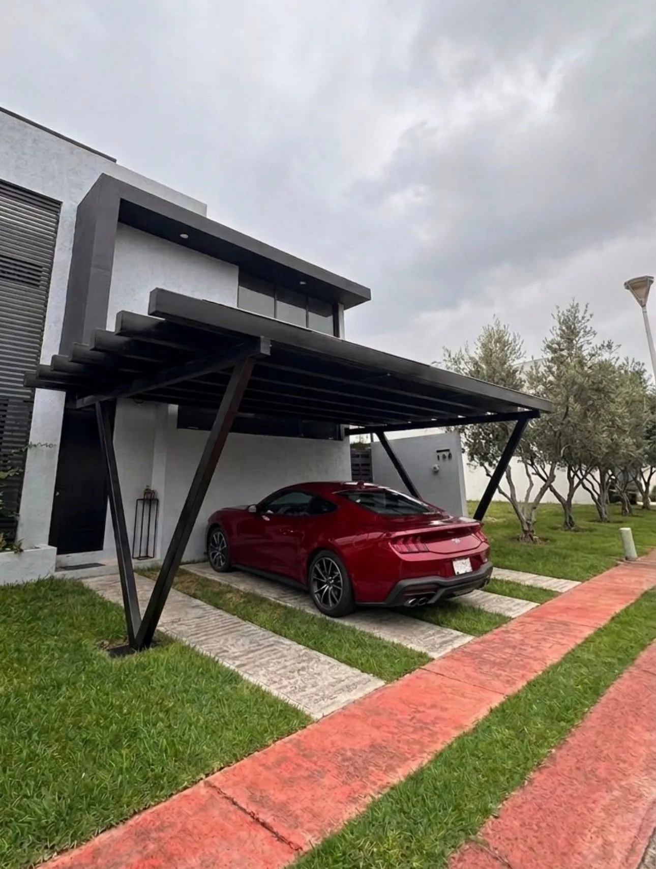 Cochera techada con estructura de herrería en acero negro, en voladizo sobre el acceso de una residencia